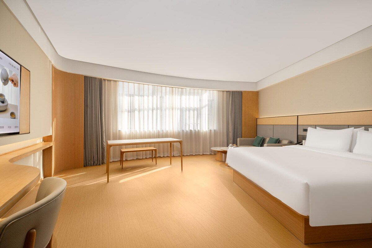 A modern hotel room with a large bed, a desk, and a chair.