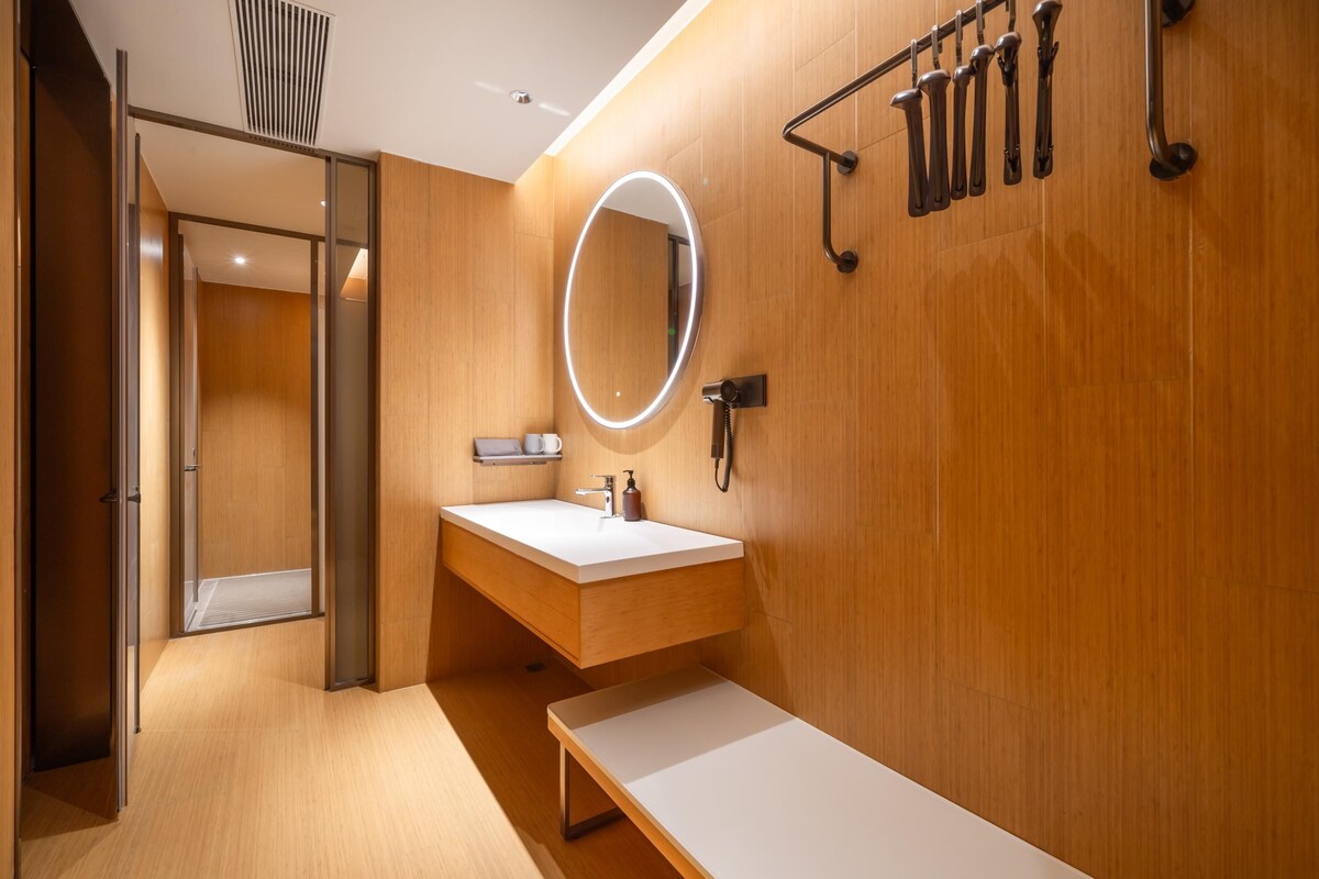 A modern bathroom with a wooden vanity, a round mirror with a light, and a towel rack.