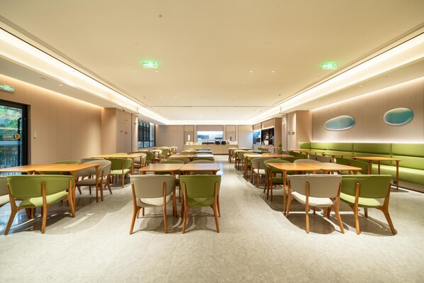 A spacious dining area with multiple tables and chairs, a green cushioned bench, and a modern ceiling design.