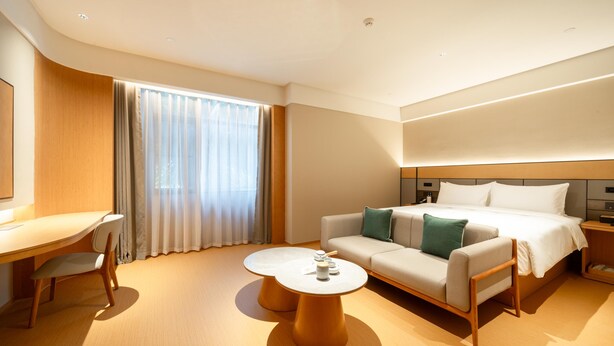 Une chambre d’hôtel moderne équipée d’un lit, d’un canapé, d’un bureau et de deux petites tables rondes.