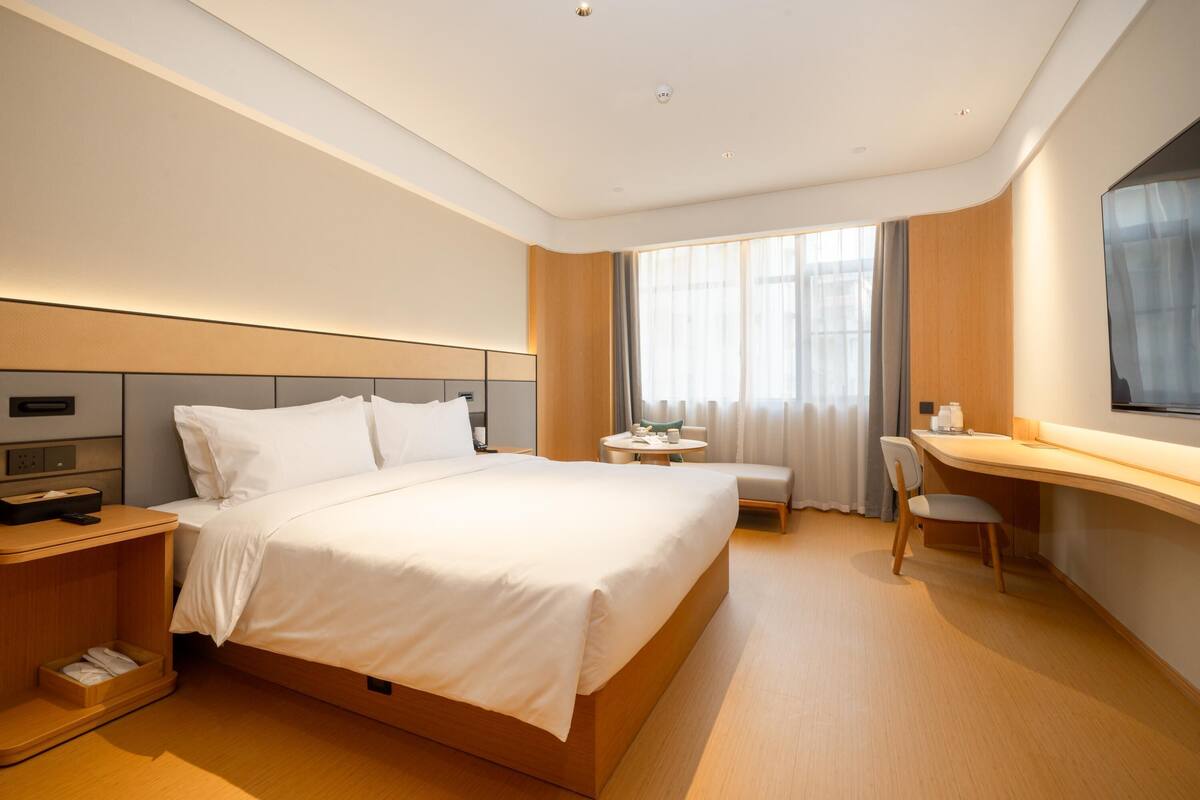 A modern hotel room with a large bed, bedside tables, a desk, and a chair.