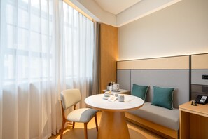 Una habitación de hotel moderna con una mesa redonda, un sofá y una mesita de noche con un teléfono.