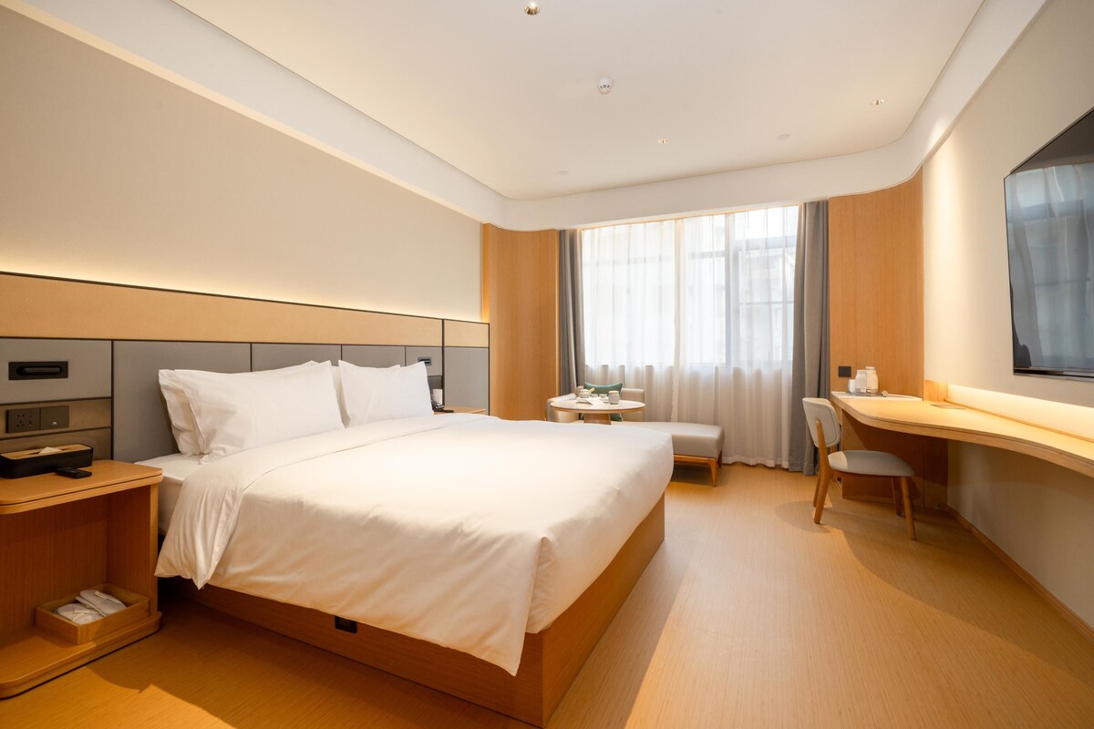 A modern hotel room with a large bed, bedside tables, a desk, and a chair.