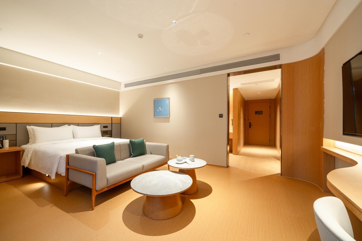 A modern hotel room with a bed, a sofa, a coffee table, and a TV.