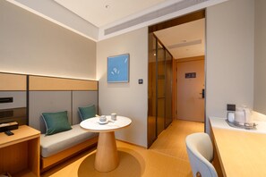 A modern hotel room with a sofa, a small round table, a chair, a bed, and a glass door leading to another room. - Ji Hotel Guangzhou Sun Yat-sen University Metro (Guangzhou)