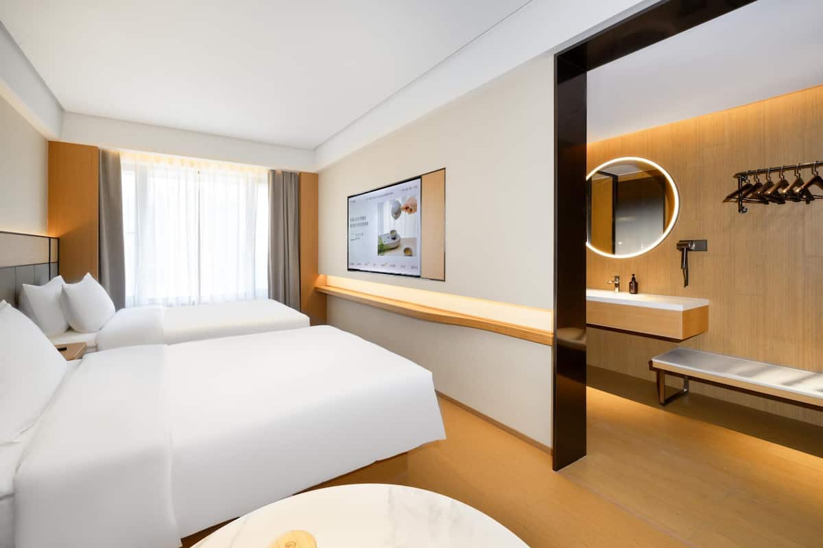 Une chambre d’hôtel avec un grand lit, une table de chevet, un miroir, un petit banc et un téléviseur fixé au mur.