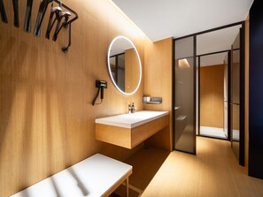 A modern bathroom with a wooden vanity, a round mirror, and a glass shower enclosure.