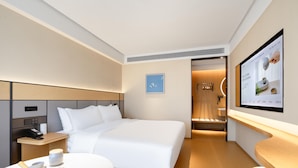 A modern hotel room with a neatly made bed, a bedside table with a phone and a cup, and a wall-mounted TV displaying a menu. - Ji Hotel Guangzhou Baiyun Tinggang Metro Station (Guangzhou)