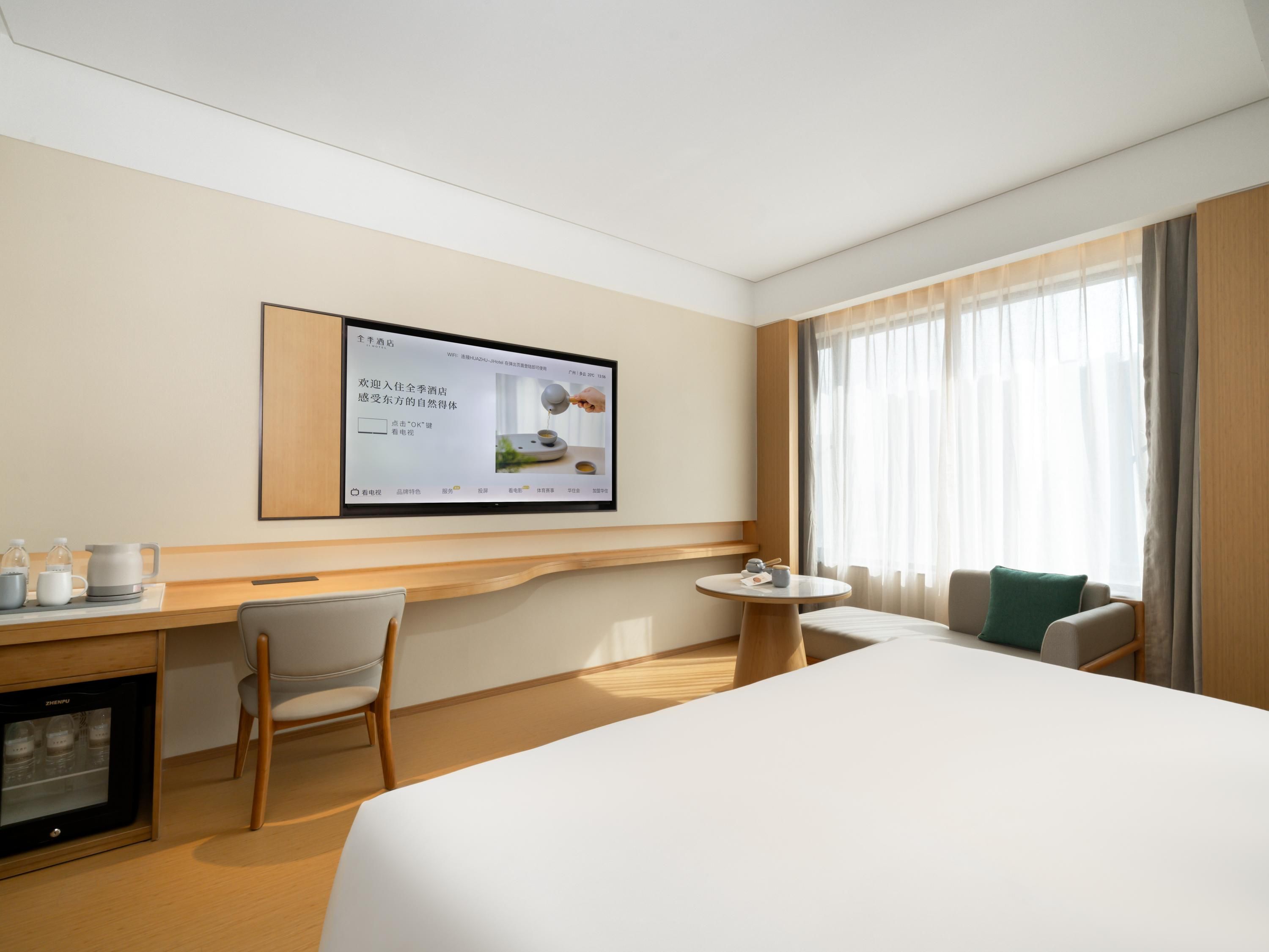 Habitación de hotel con cama, escritorio, silla, mesita y televisor montado en la pared.