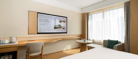A hotel room with a bed, a desk, a chair, a small table, and a television mounted on the wall.