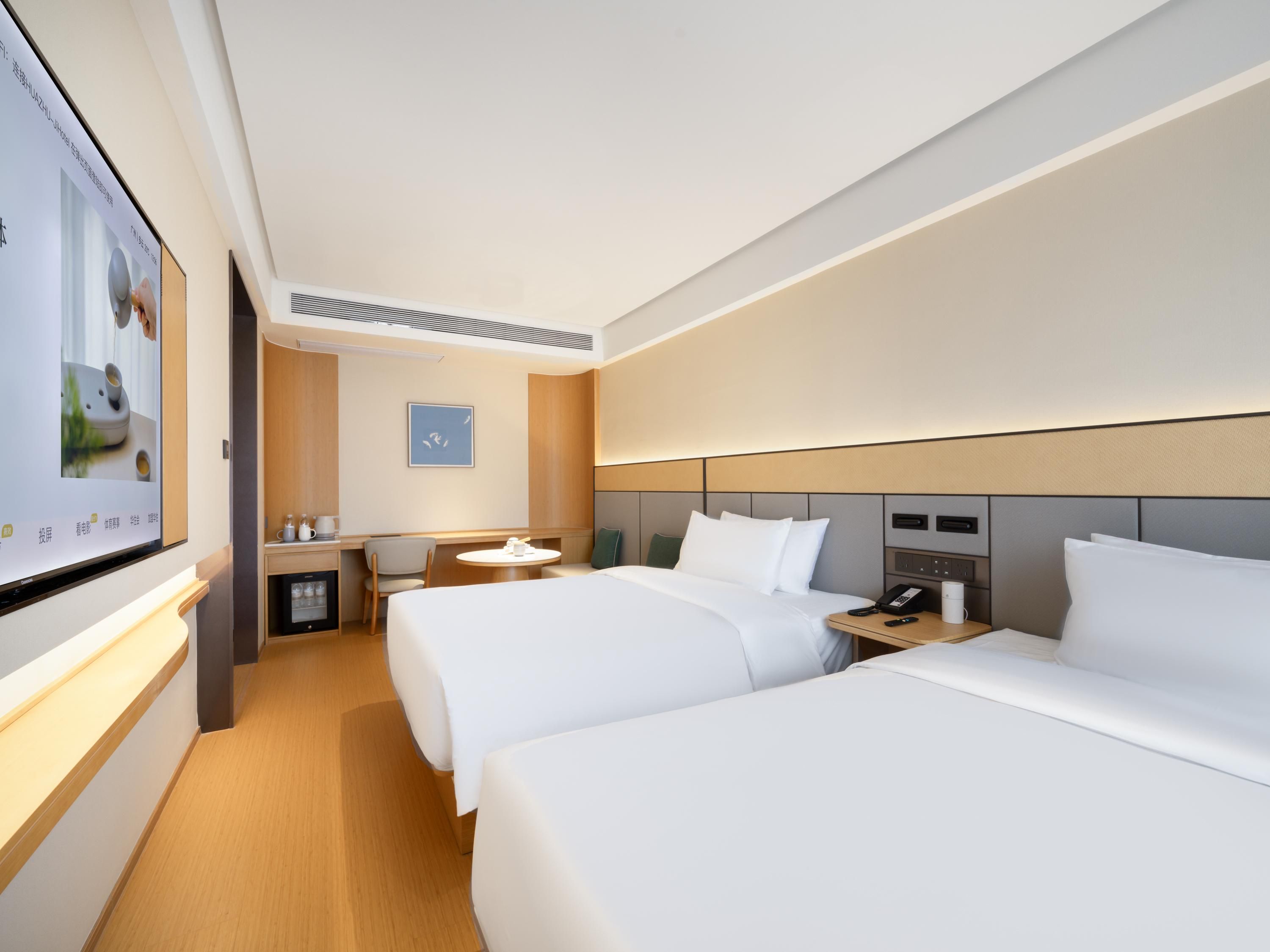 Ein modernes Hotelzimmer mit zwei Betten, einem Schreibtisch, einem Sessel, einem kleinen Tisch und einem Fernseher.