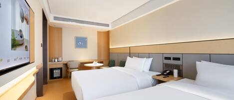 Ein modernes Hotelzimmer mit zwei Betten, einem Schreibtisch, einem Sessel, einem kleinen Tisch und einem Fernseher.