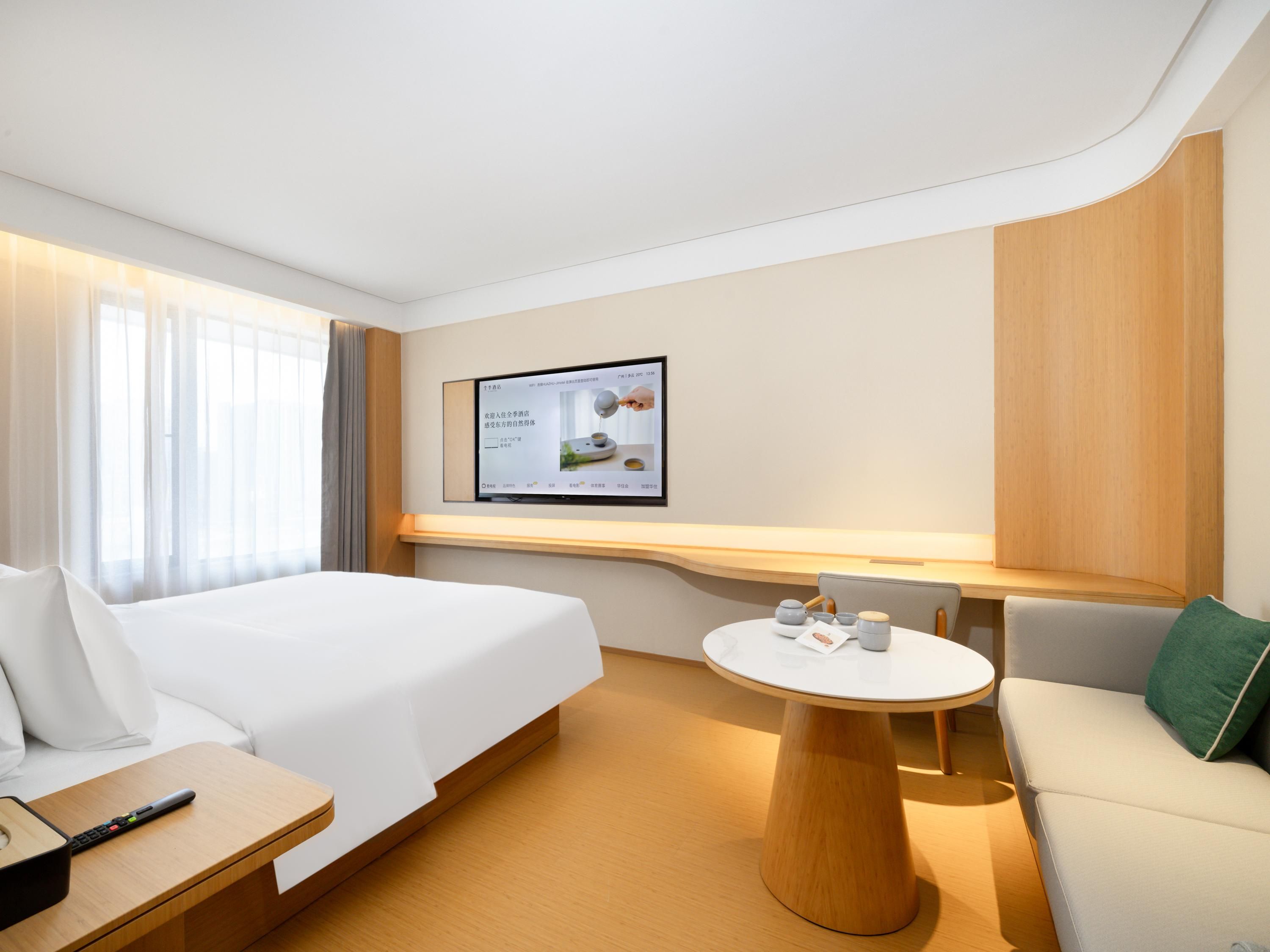 A hotel room with a bed, a desk, a round table, and a TV mounted on the wall.