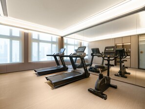 Une salle de sport moderne équipée de tapis de course, de vélos elliptiques et d’un mur recouvert de miroirs.