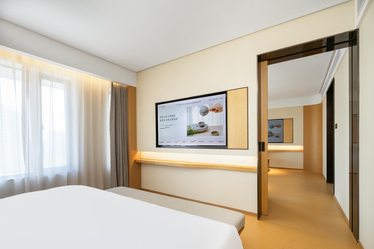 A hotel room with a bed, a TV mounted on the wall, and a wooden door leading to another room.