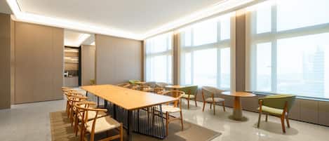 A spacious conference room with a long table and chairs, large windows, and a high ceiling.