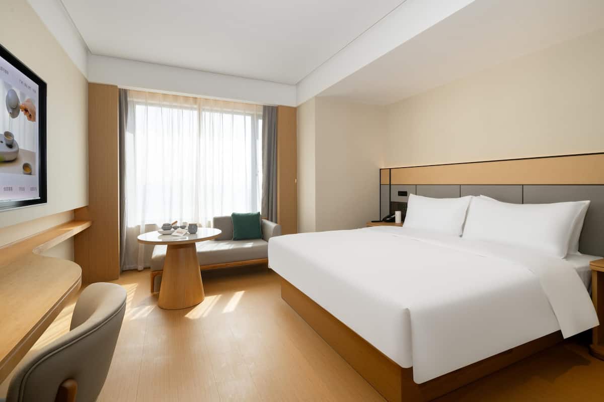 Une chambre d’hôtel avec un grand lit, une petite table ronde, un canapé et un téléviseur fixé au mur.