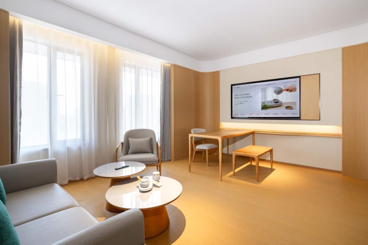 Une chambre d’hôtel moderne, équipée d’un canapé, de deux tables rondes, d’une chaise et d’un téléviseur fixé au mur.