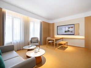 A modern hotel room with a sofa, two round tables, a chair, and a TV mounted on the wall.