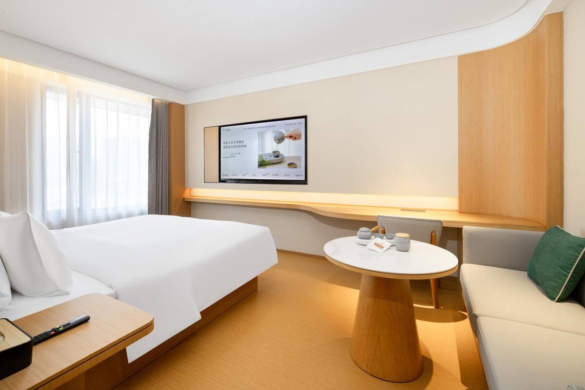 Une chambre d’hôtel équipée d’un lit, d’un bureau, d’une table ronde et d’un téléviseur fixé au mur.