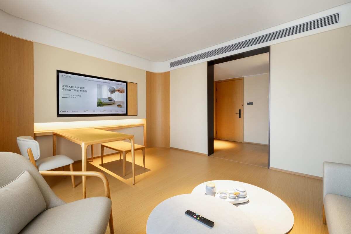 Ein modernes Hotelzimmer mit einem Wand-Fernseher, einem Holztisch, einem runden Couchtisch und einem Sofa.