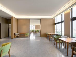 Un comedor moderno y luminoso, con techos altos y ventanas amplias, que presenta sillas y mesas en tonos verde y beige.
