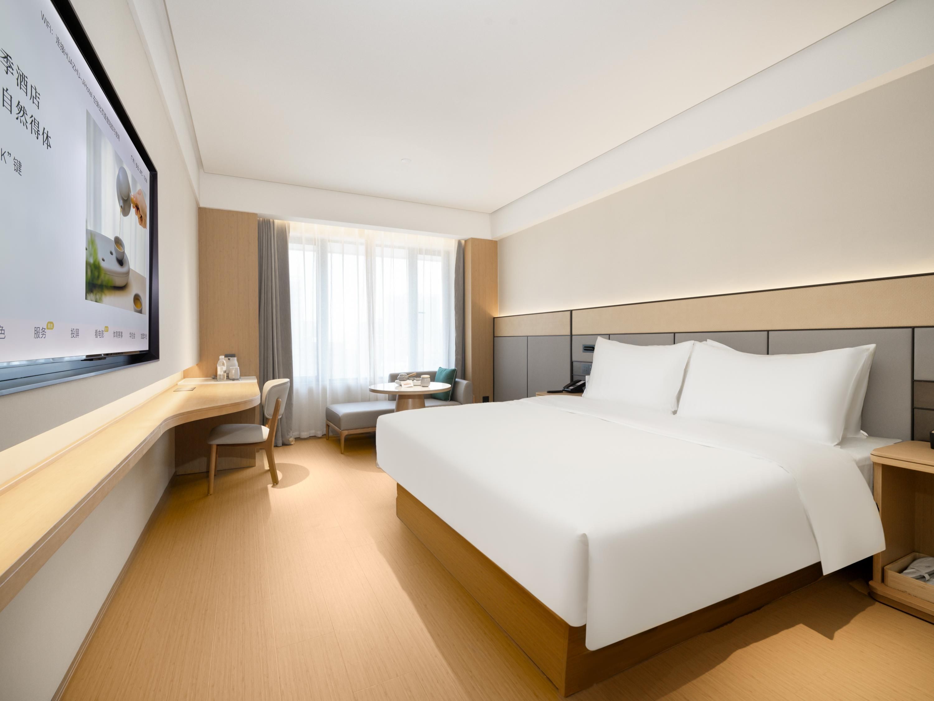 A hotel room with a large bed, a desk, and a television on the wall.