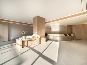 A modern hotel lobby with a reception desk, seating area, and a large pillar.