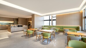 A modern dining area with a central island, green cushioned seating, and a kitchen in the background. - Ji Hotel Guangzhou Baiyun Tinggang Metro Station (Guangzhou)