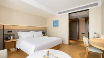 Quarto de hotel com cama, mesa de cabeceira, cadeira e pequena mesa de jantar com chaleira e xícaras.