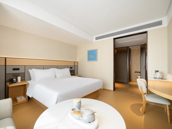 Una habitación de hotel con cama, mesita de noche, silla y una pequeña mesa de comedor con tetera y tazas.