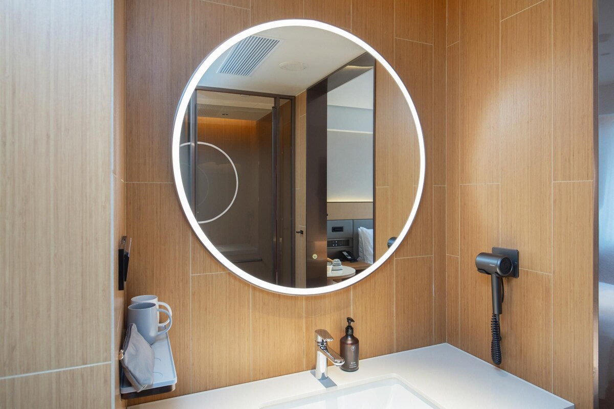 A modern bathroom with a round mirror, a hairdryer, and a towel rack.