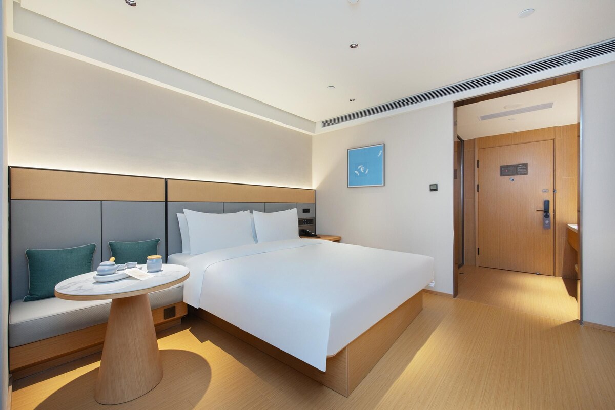 A modern hotel room with a large bed, a small round table, and a sofa with cushions.