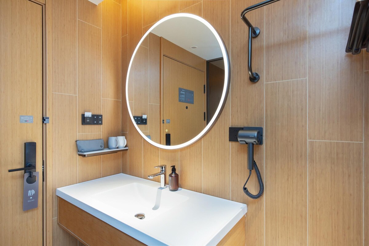 A modern bathroom with a white sink, a round mirror, a towel rack, and a shower area.