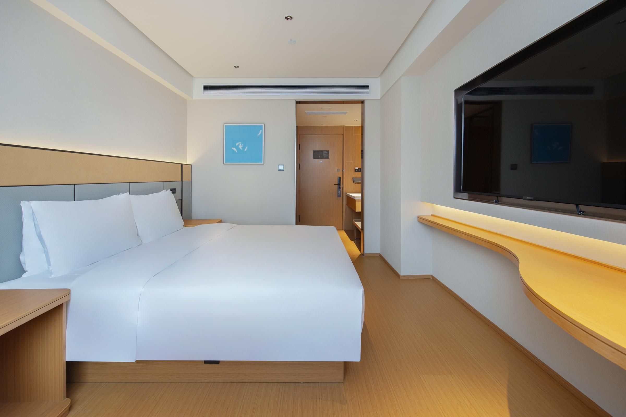 A hotel room with a large bed, a wooden nightstand, a TV, and a wooden counter.