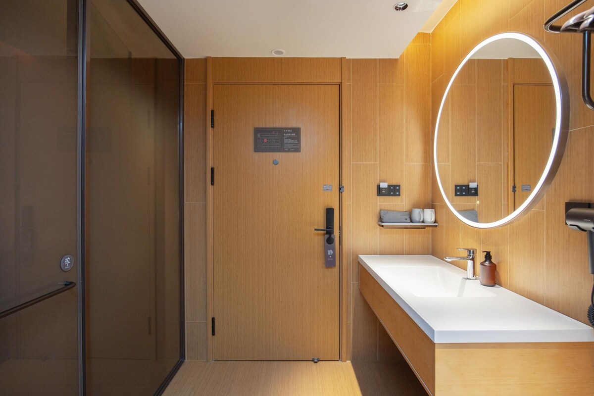 A modern bathroom with a wooden door, a white sink, and a mirror with a circular light.