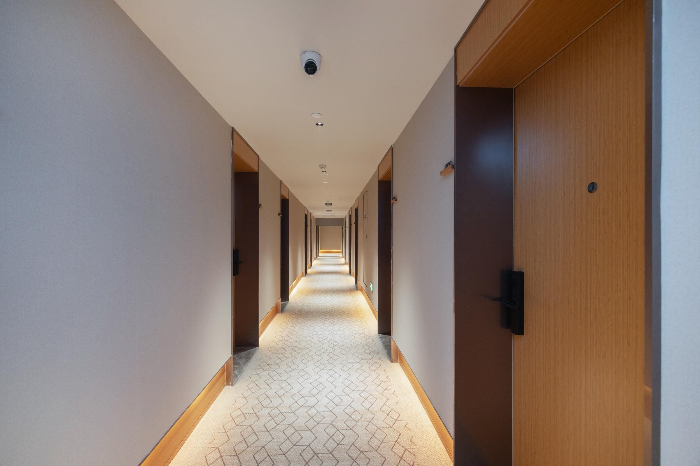 A hotel hallway with a patterned carpet, wooden doors, and recessed lighting.