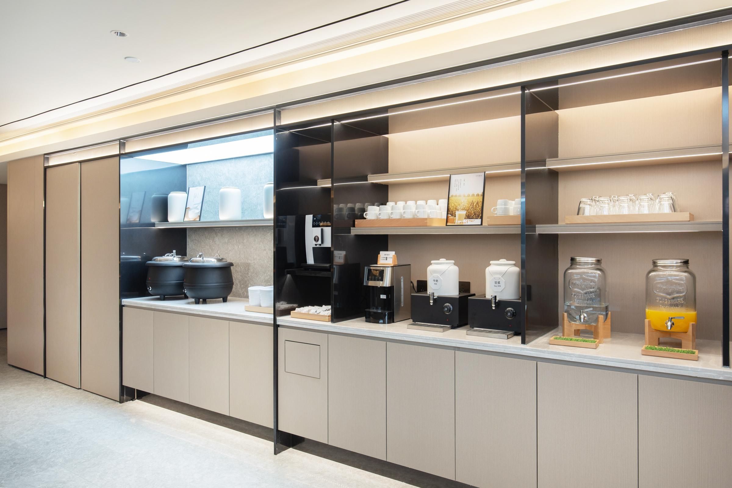 A modern kitchen area with coffee machines, tea dispensers, and storage shelves.