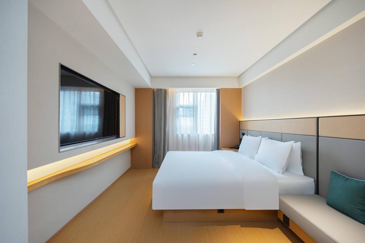 Une chambre d’hôtel moderne, dotée d’un grand lit, d’une table de chevet, d’une fenêtre avec des rideaux et offrant une vue sur l’extérieur.