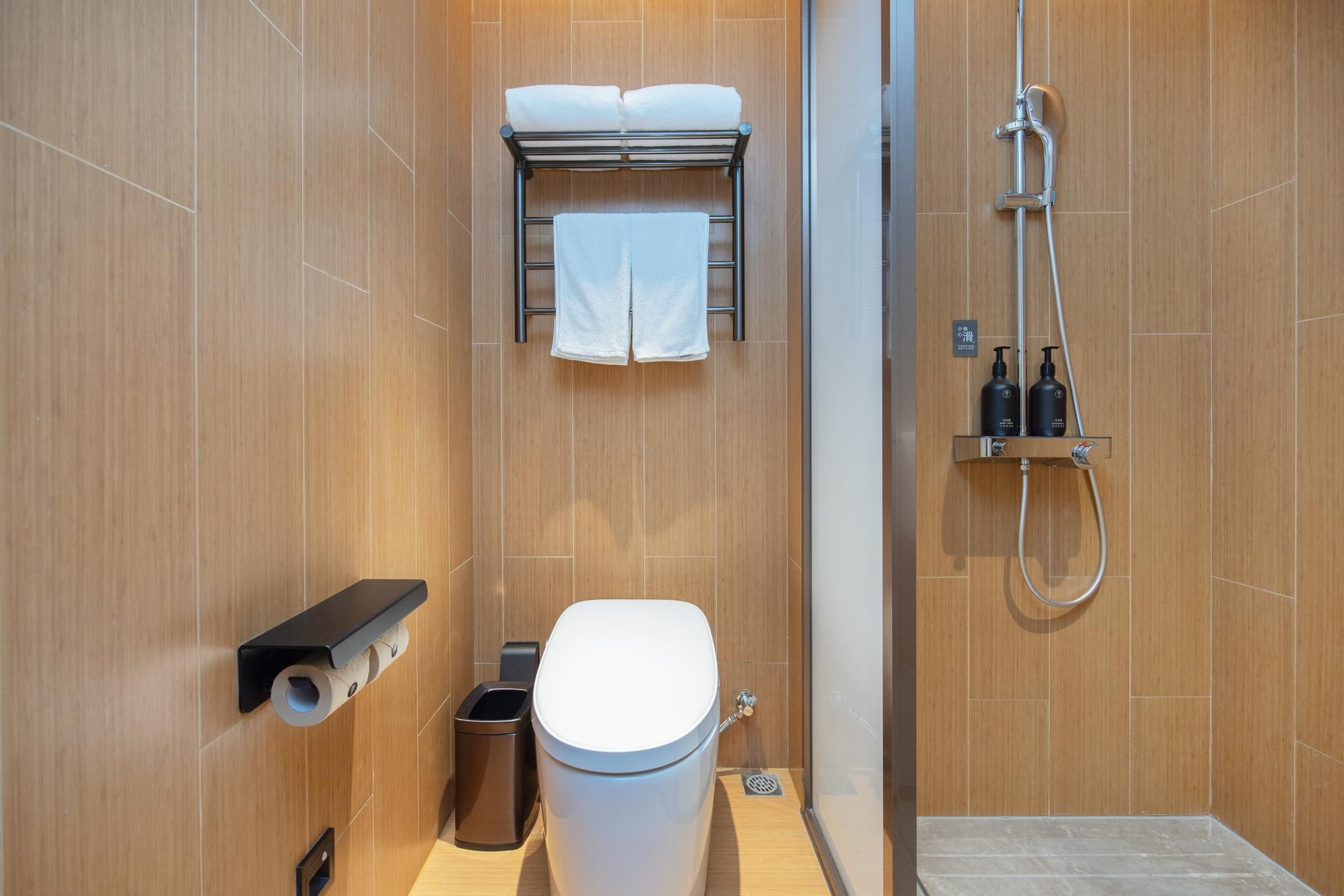 A modern bathroom with a toilet, towel rack, shower, and toiletries.