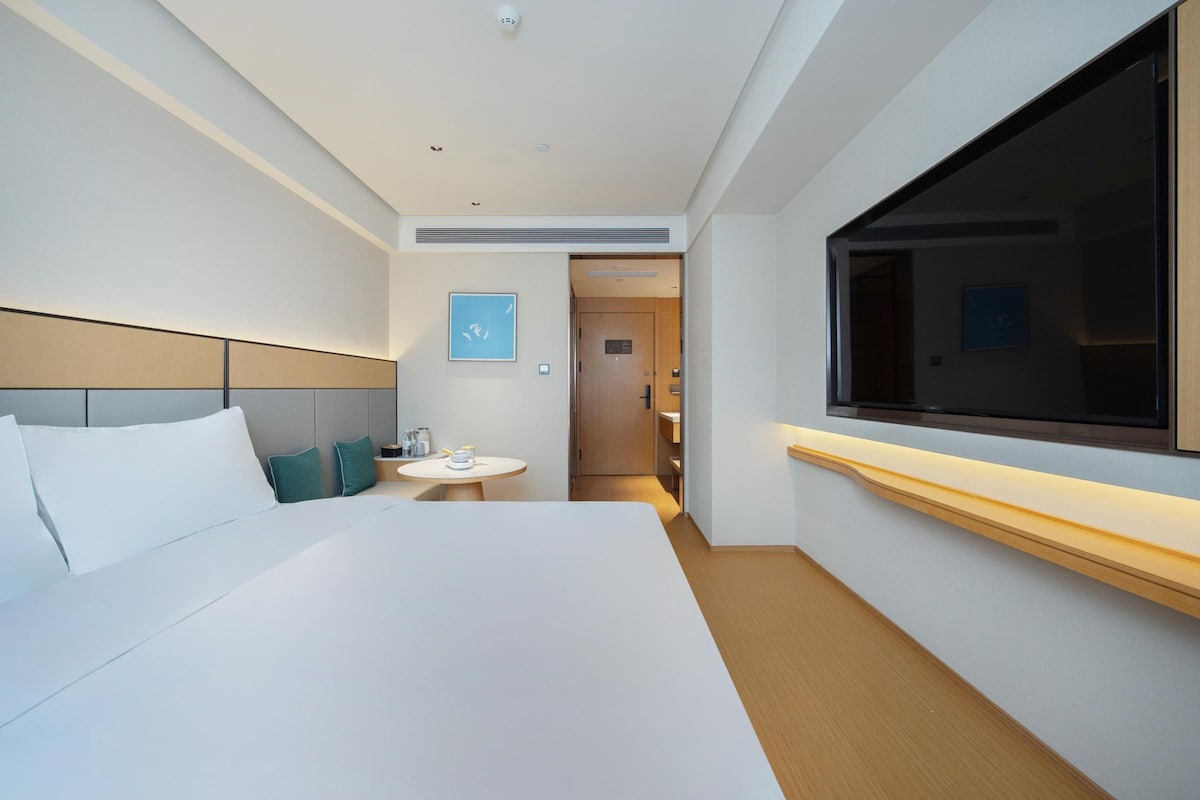A modern hotel room with a large bed, a bedside table, a TV, and a small round table.