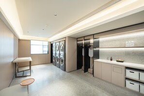 A modern hotel room with a large window, a built-in washer and dryer, a vanity with a mirror, and a small seating area. - Ji Hotel Guangzhou Modiesha Metro Station (Guangzhou)