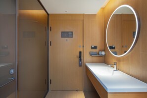 A modern bathroom with a wooden door, a built-in sink, and a mirror with a circular light. - Ji Hotel Guangzhou Modiesha Metro Station (Guangzhou)