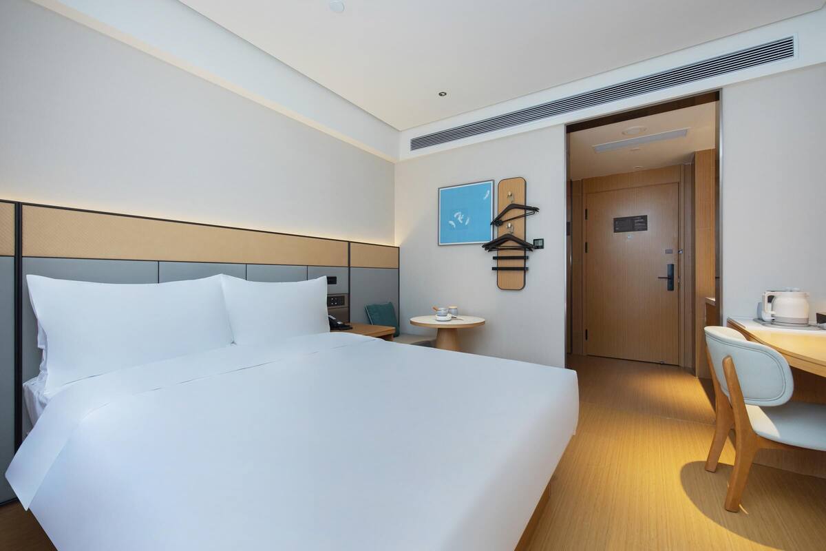 Une chambre d’hôtel avec un grand lit, un bureau, une chaise, une petite table ronde et un porte-manteau fixé au mur.