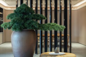 A modern interior with a large potted plant, a wooden table with a decorative item, and a seating area with chairs and a table. - Ji Hotel Guangzhou Modiesha Metro Station (Guangzhou)