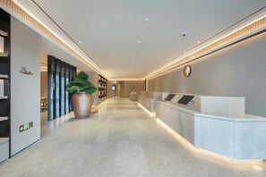 A modern hotel reception area with a marble floor, a reception desk, a large potted plant, and a wall-mounted clock. - Ji Hotel Guangzhou Modiesha Metro Station (Guangzhou)