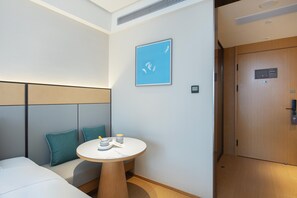 A hotel room with a bed, a small round table with a cup and saucer, a blue wall art, and a wooden door. - Ji Hotel Guangzhou Modiesha Metro Station (Guangzhou)