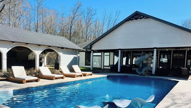 A swimming pool with lounge chairs, a covered patio, and a slide.