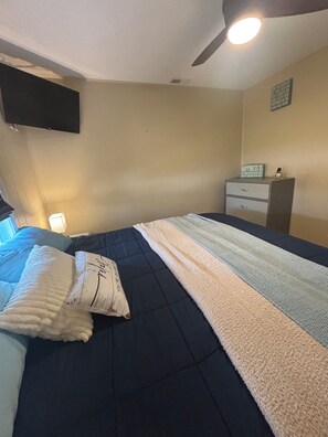 Un dormitorio con cama, mesita de noche, televisor en la pared y ventilador de techo.