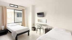 Une chambre d’hôtel avec deux lits, un bureau, une chaise, une télévision et une fenêtre avec des rideaux.